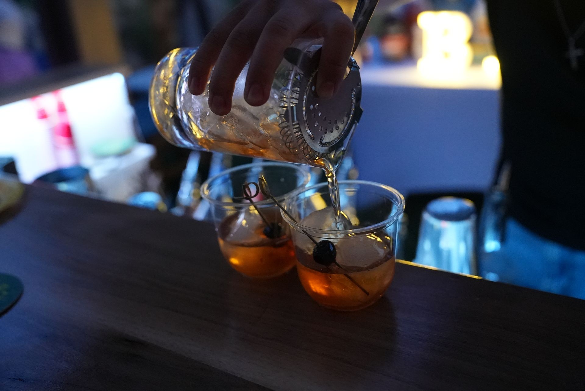 Bartender pouring cocktails from a shaker into two glasses on a bar counter.