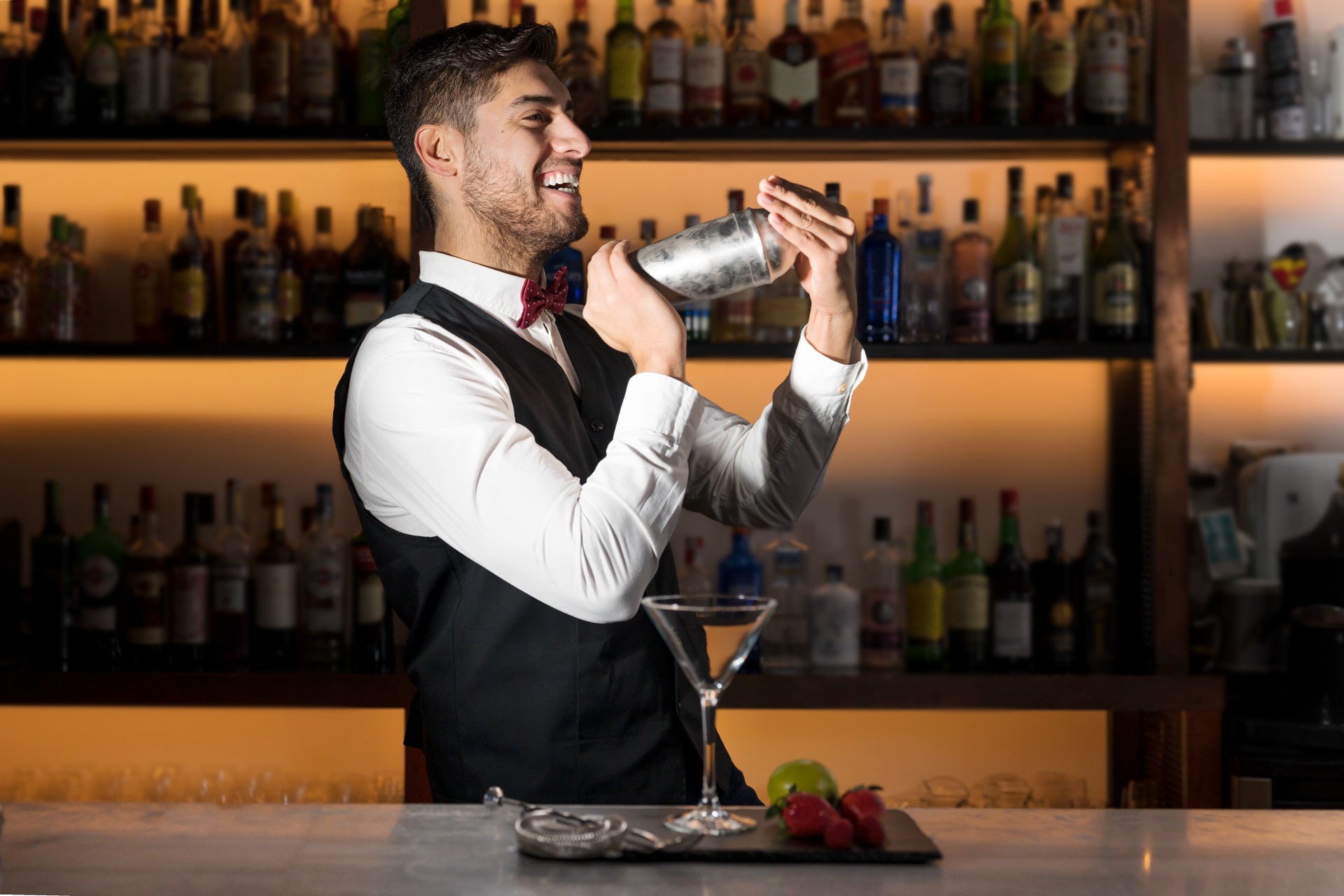 Cool professional bartender making a cocktail, shaking a cocktail shaker. Authentic barman making alcohol beverages in modern bar.